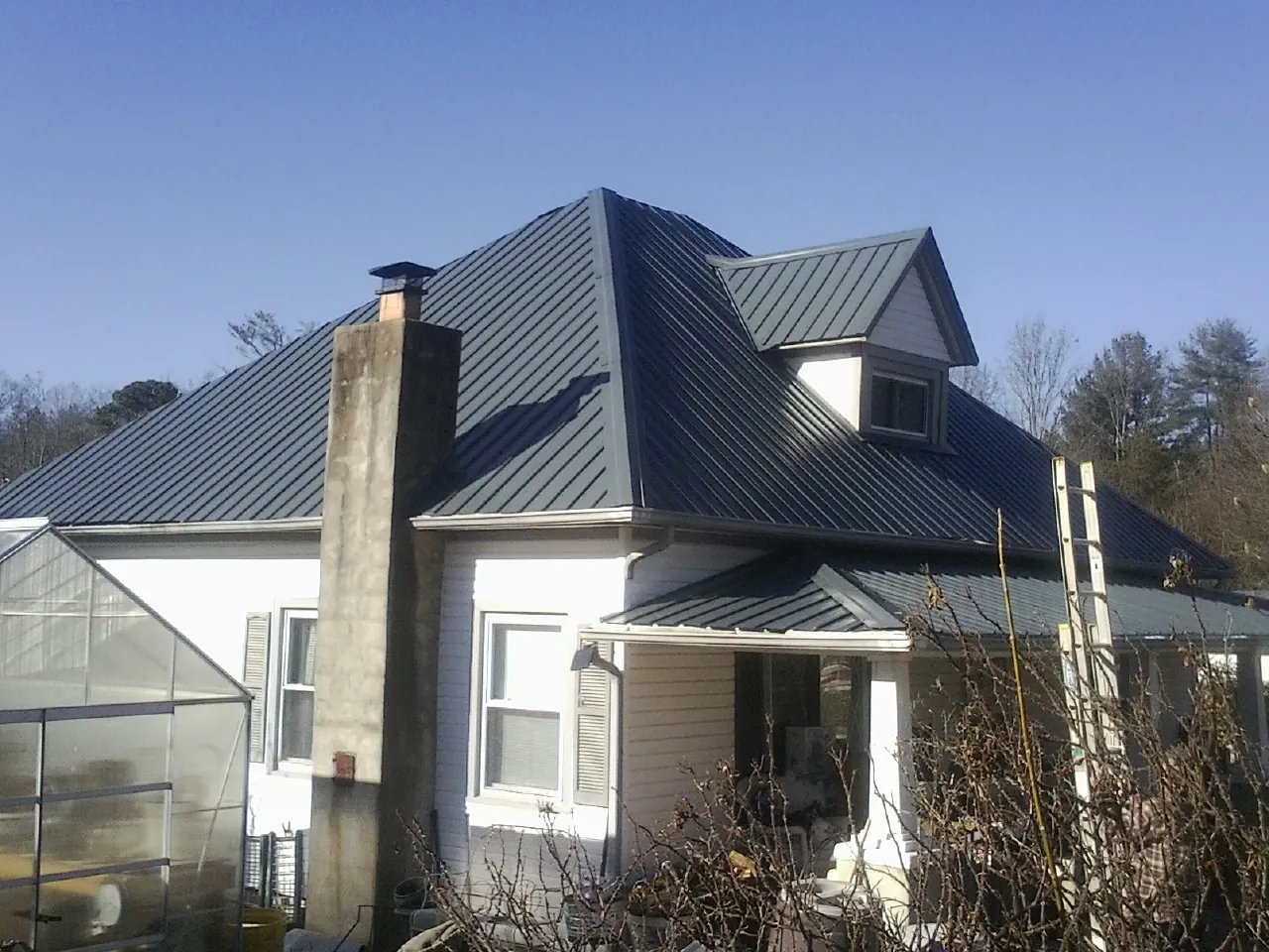 Dark blue standing seam metal roof on a white farmhouse with dormer — Slate & Tile Roof Repair by Roofing Brothers in Warrensville