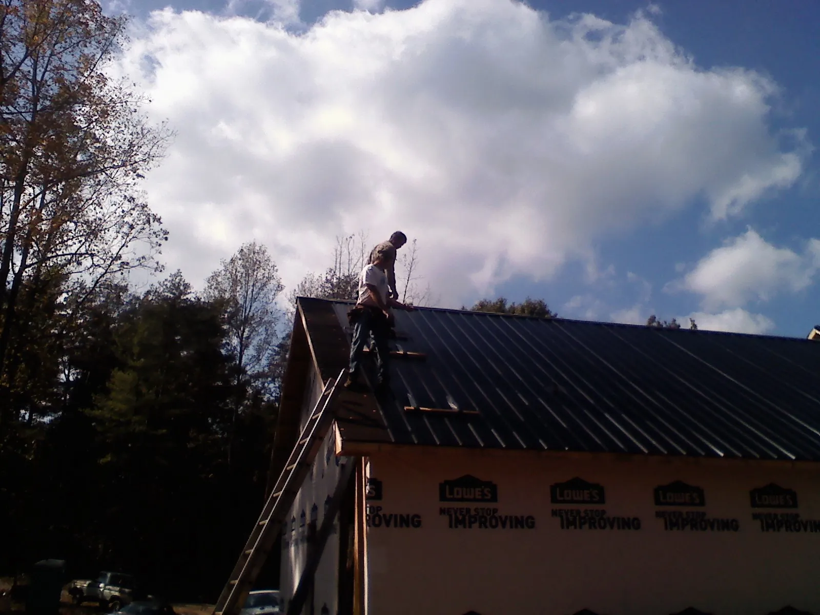 Roofer fastening dark metal panels high against a cloudy sky, from a Roof Inspection job in Warrensville