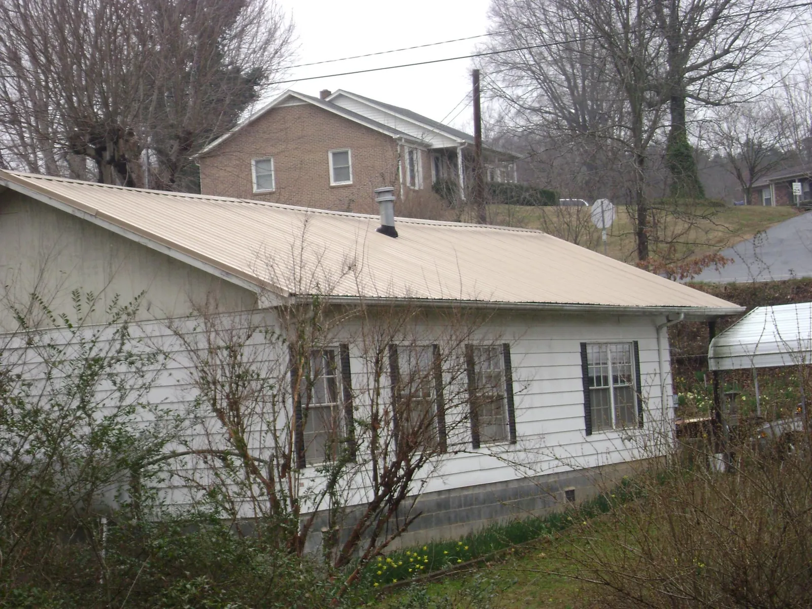 Tan metal roof on a white sided house set into a hillside — Commercial Roofing by Roofing Brothers in Warrensville